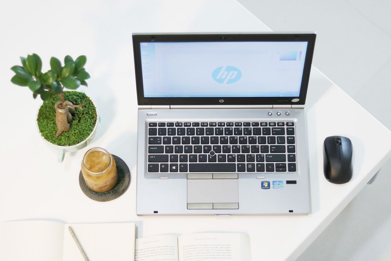 our-services-1 Aerial view of a modern workspace featuring a laptop, plant, and iced coffee in a minimalist setting.